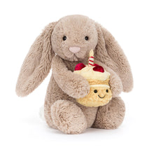 Load image into Gallery viewer, Jellycat Bashful Beige Bunny | Birthday Plush bunny holding a cupcake with a candle on a white background
