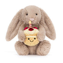 Load image into Gallery viewer, Jellycat Bashful Beige Bunny | Birthday Plush toy rabbit holding a cupcake with a candle on a white background
